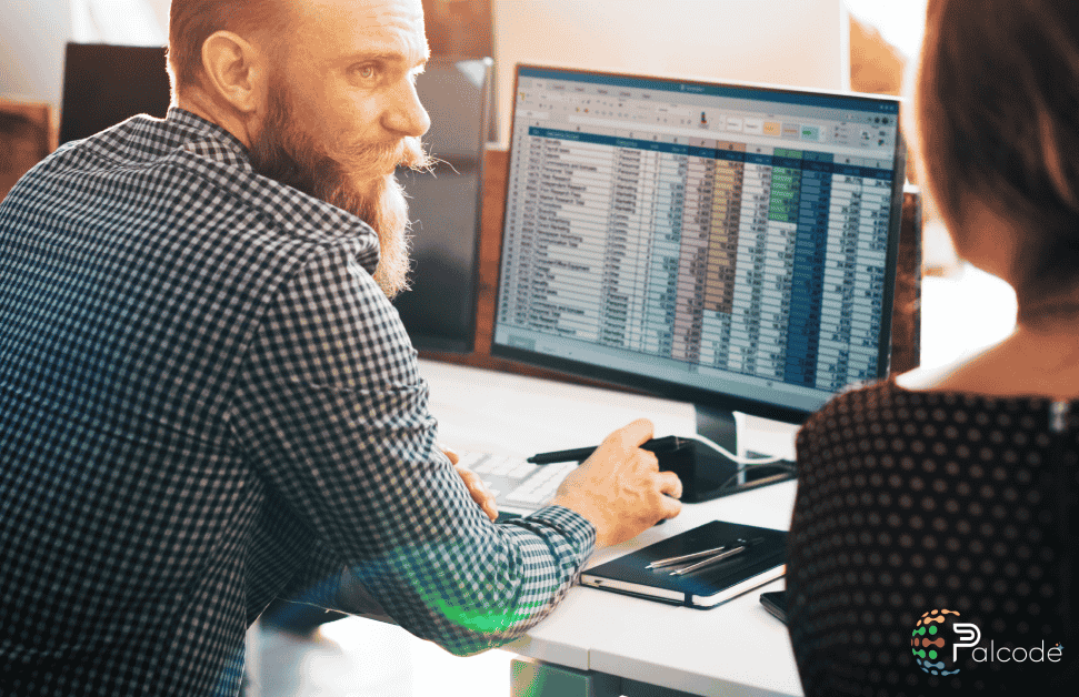 A man and woman collaborate at a desk reviewing a computer screen displaying Construction Bid Management software